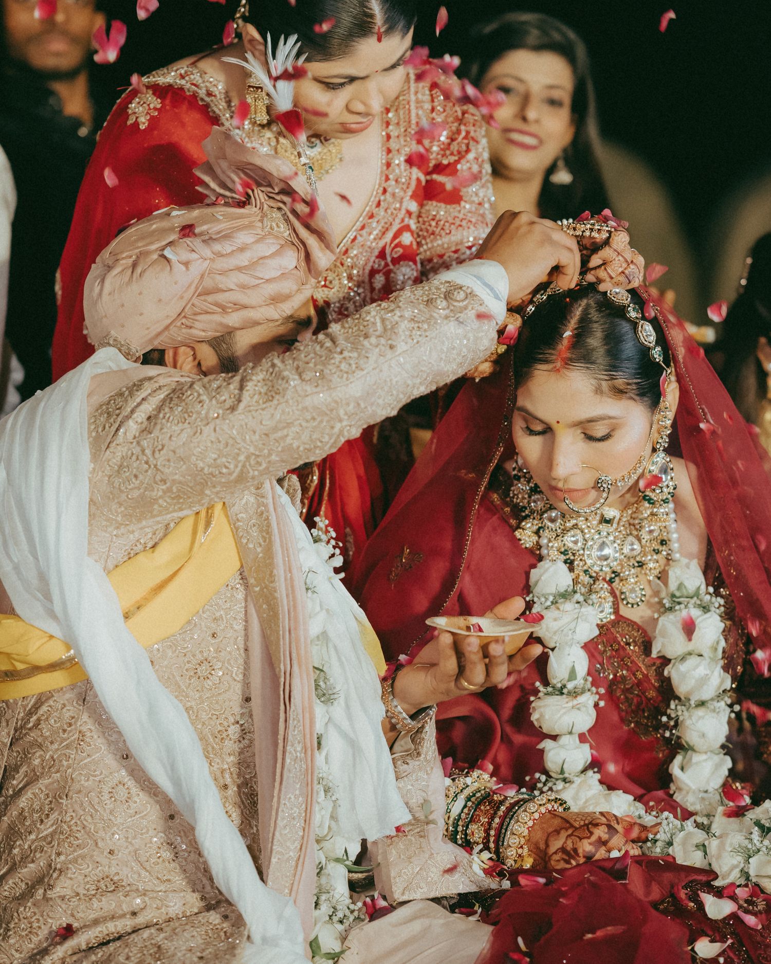 Groom applying sindoor to bride during traditional Indian wedding ceremony, both adorned in rich red and gold bridal attire.