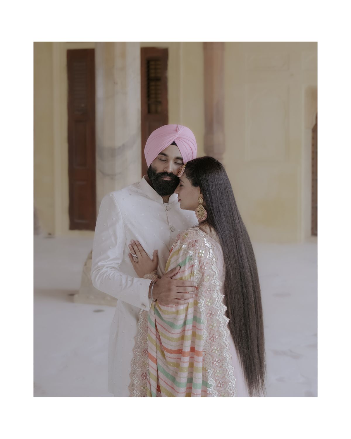 Romantic couple portrait in traditional Indian attire against a light colored architectural backdrop.