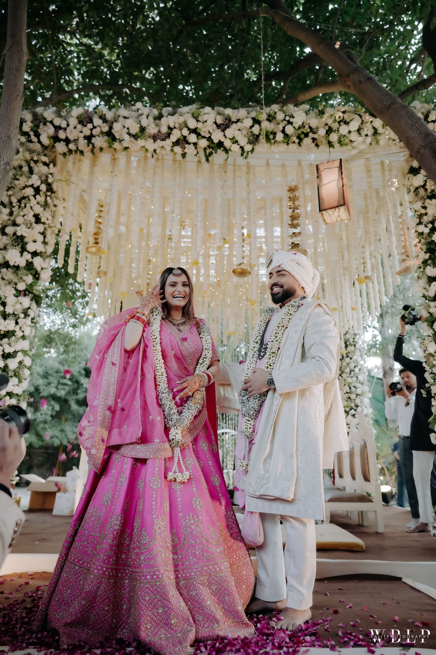 Traditional Indian wedding ceremony under a floral mandap with white flowers and hanging crystal decorations.