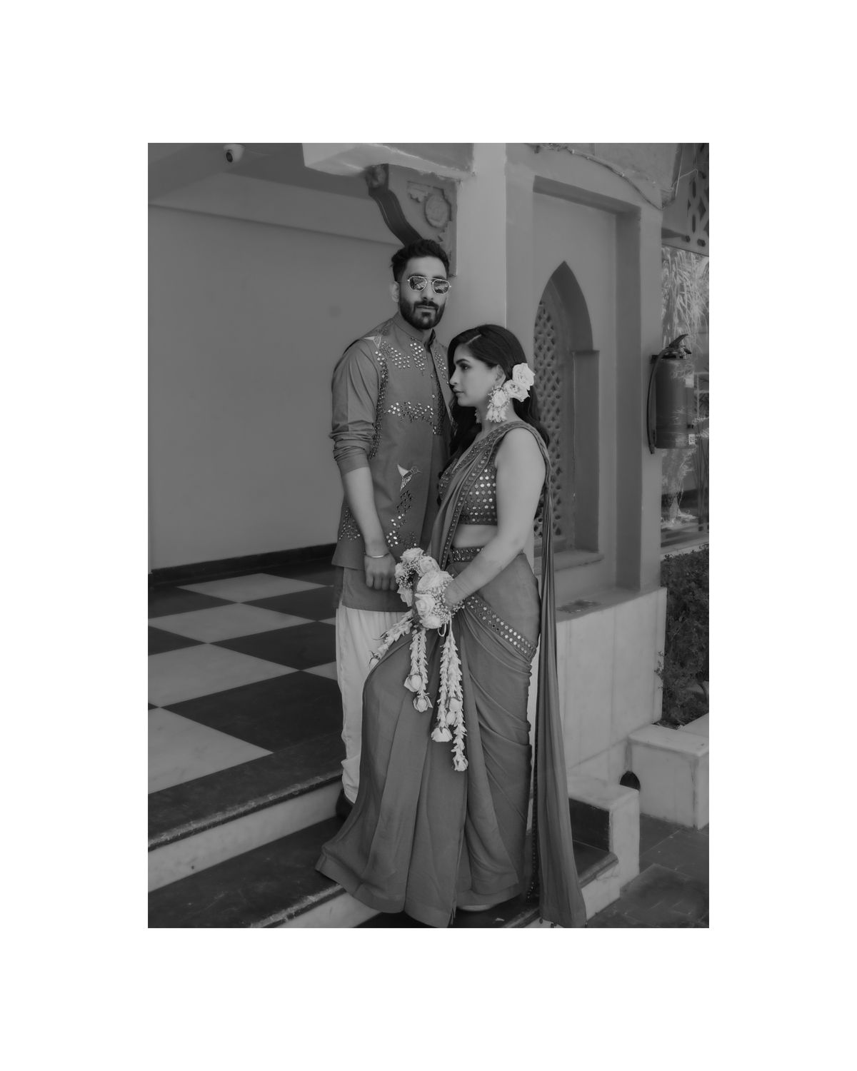 Couple in traditional Indian attire posing on a checkered floor.