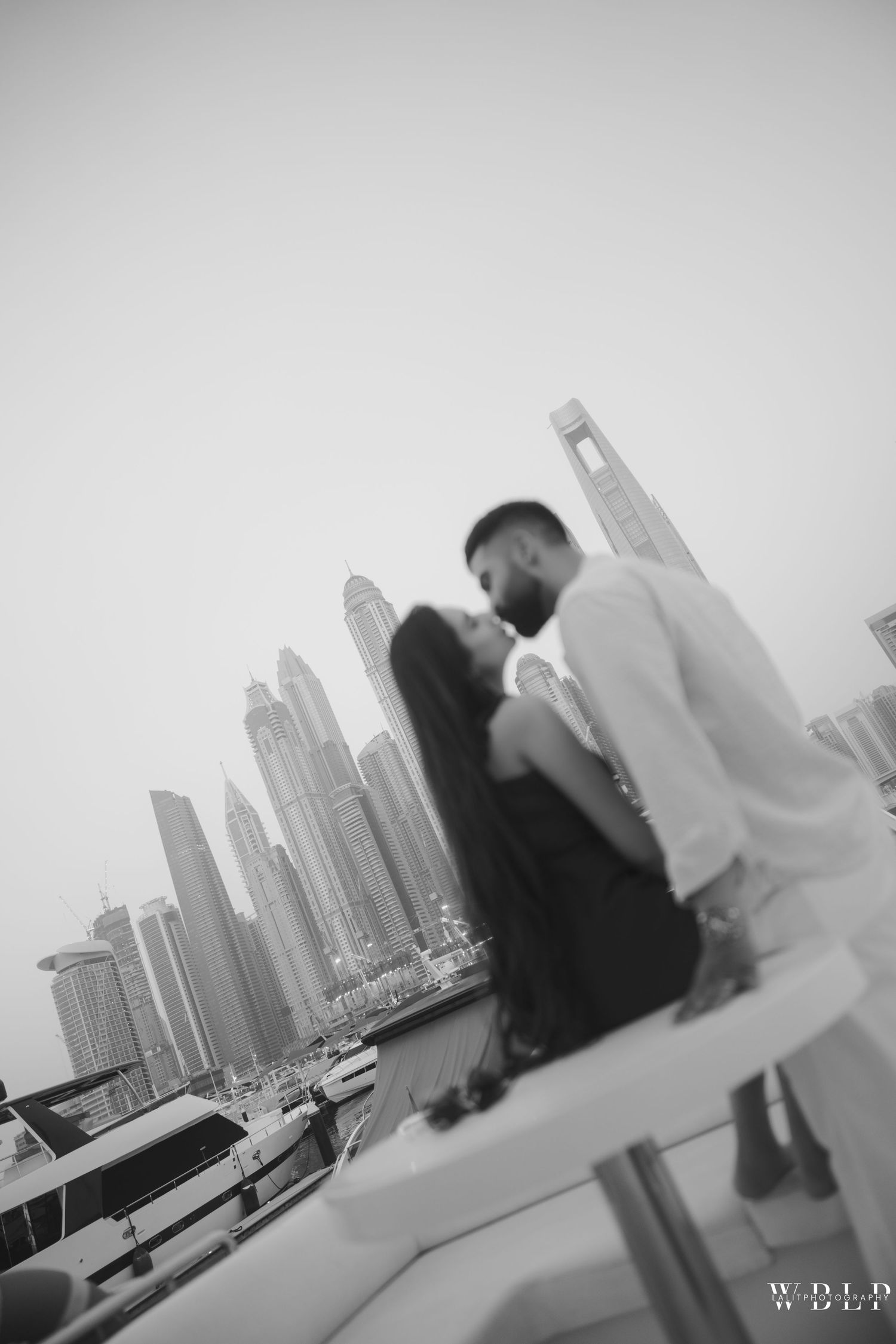 Black and white photo of a couple sharing a romantic moment on a yacht with Dubai Marina skyline in the background.