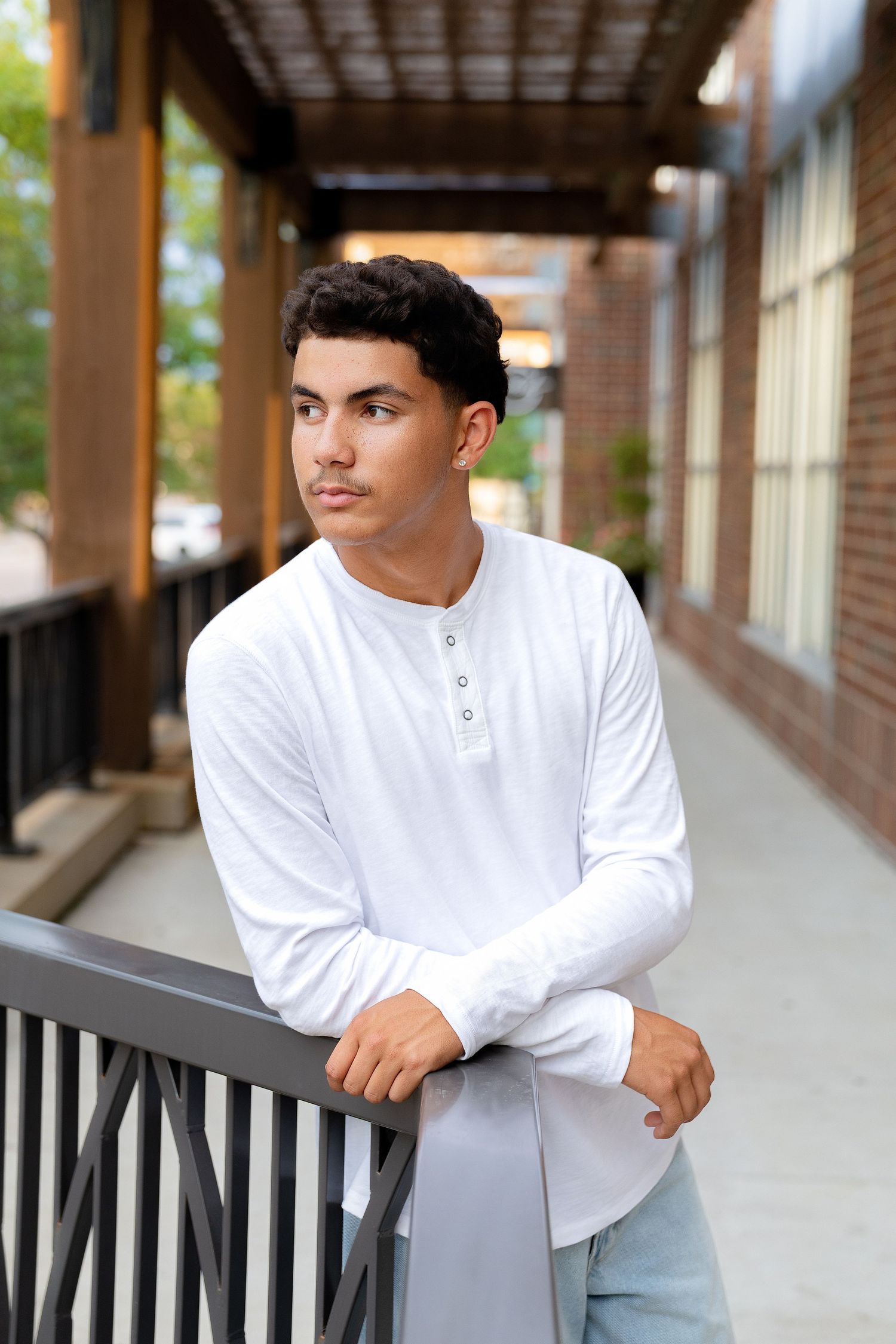 Young man in white henley shirt leaning on railing outdoors.