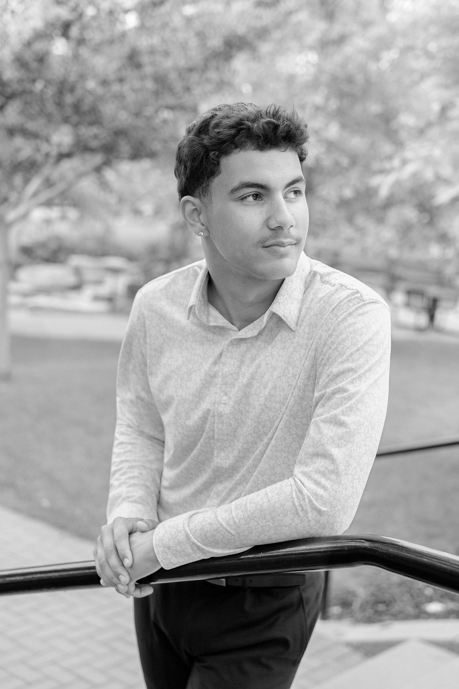 Young man in button-up shirt leaning on railing outdoors, black and white portrait photo.