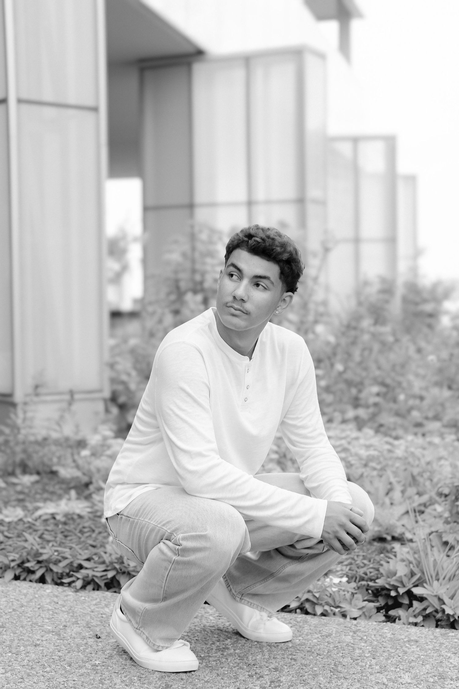 Black and white portrait of young man crouching outdoors near building.