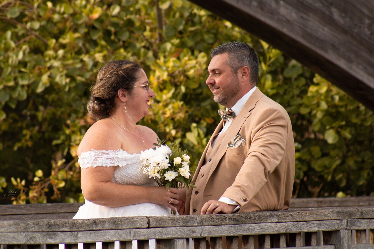 Newlyweds gazing lovingly at each other on a rustic wooden bridge surrounded by autumn leaves.