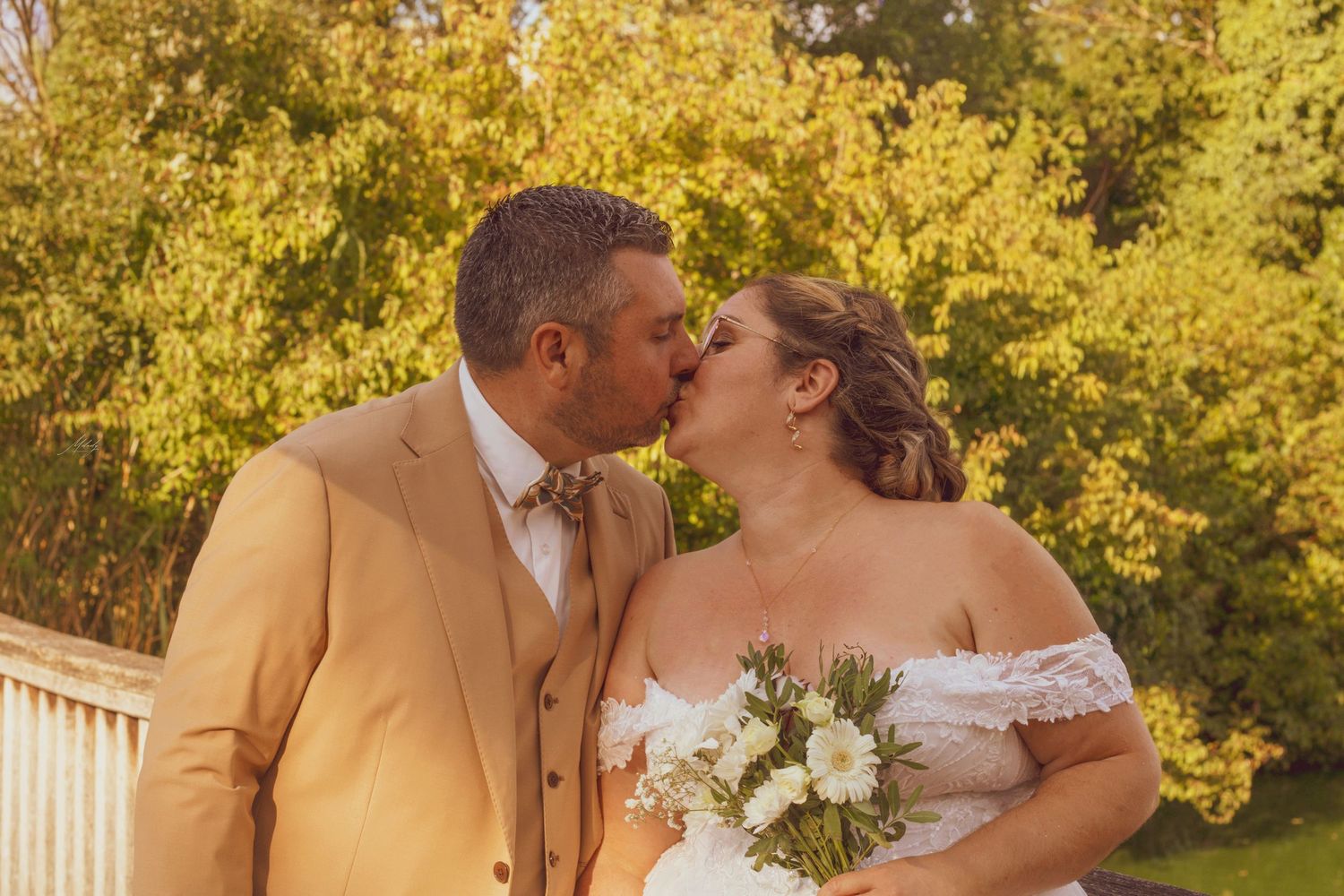 Bride and groom sharing a romantic kiss outdoors with golden autumn foliage in the background.