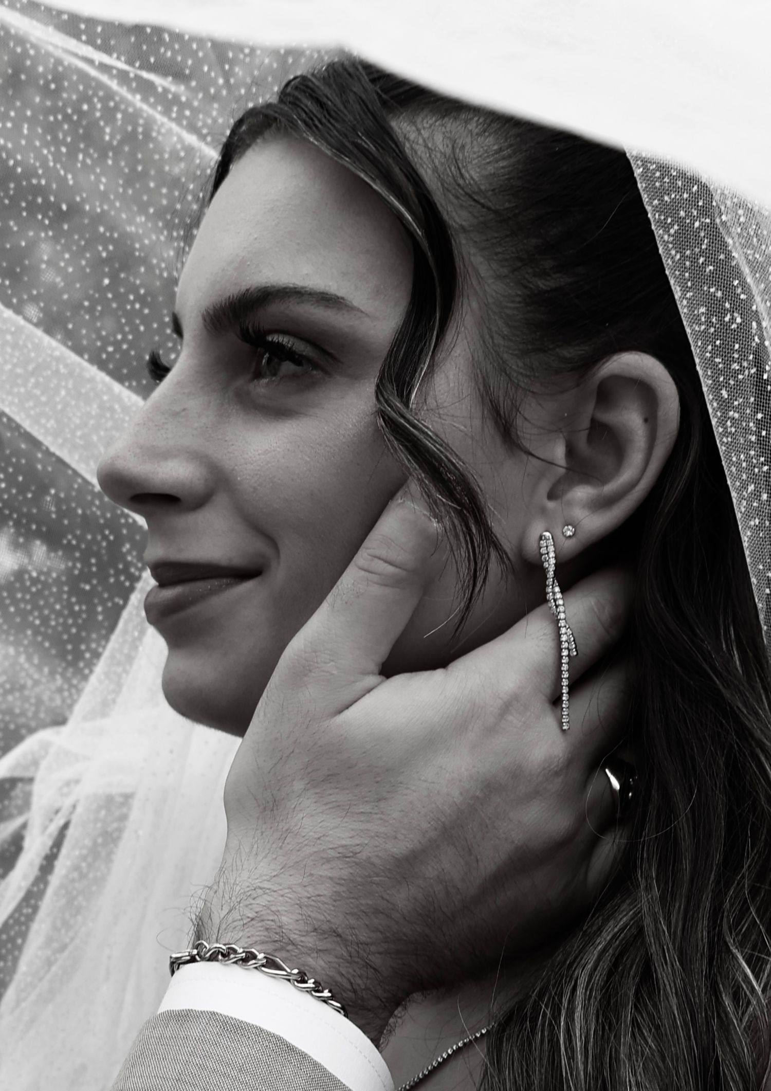 Elegant black and white close-up of bride smiling under veil, groom gently touching her face.