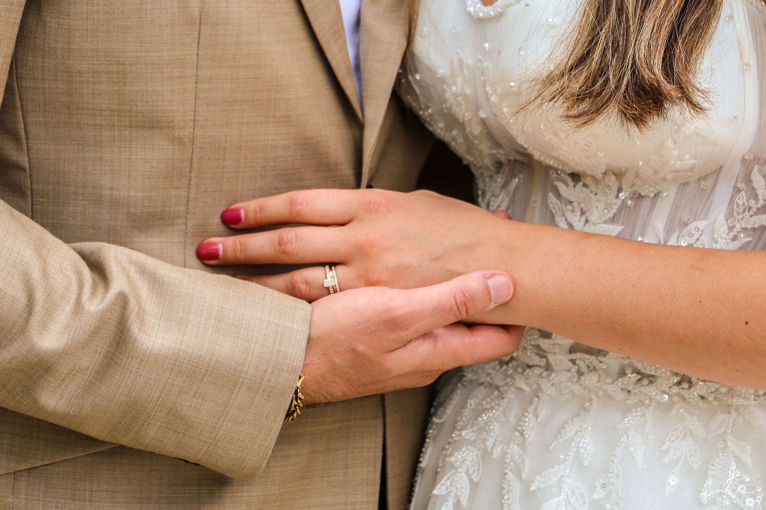 Close-up of bride and groom holding hands, showcasing gold wedding ring on bride's finger.