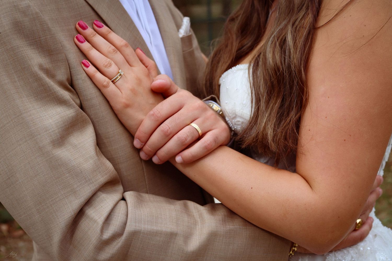 Close-up of bride and groom's hands intertwined, displaying wedding bands in elegant attire.