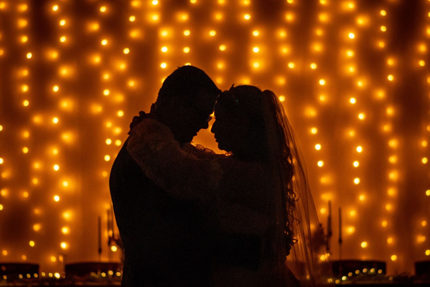 Romantic silhouettes against warm glowing string lights creating magical ambiance. Whitney McLaren Photography