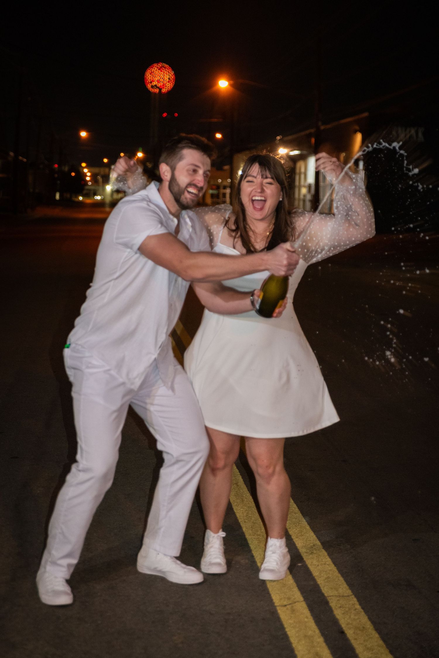 Wedding party having fun and posing playfully in white outfits at night. Whitney McLaren Photography