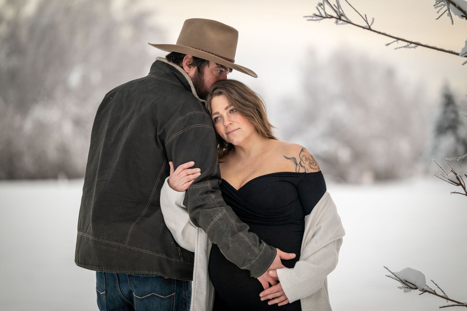 Romantic winter engagement photoshoot in a snowy forest with couple sharing intimate moments in warm coats.