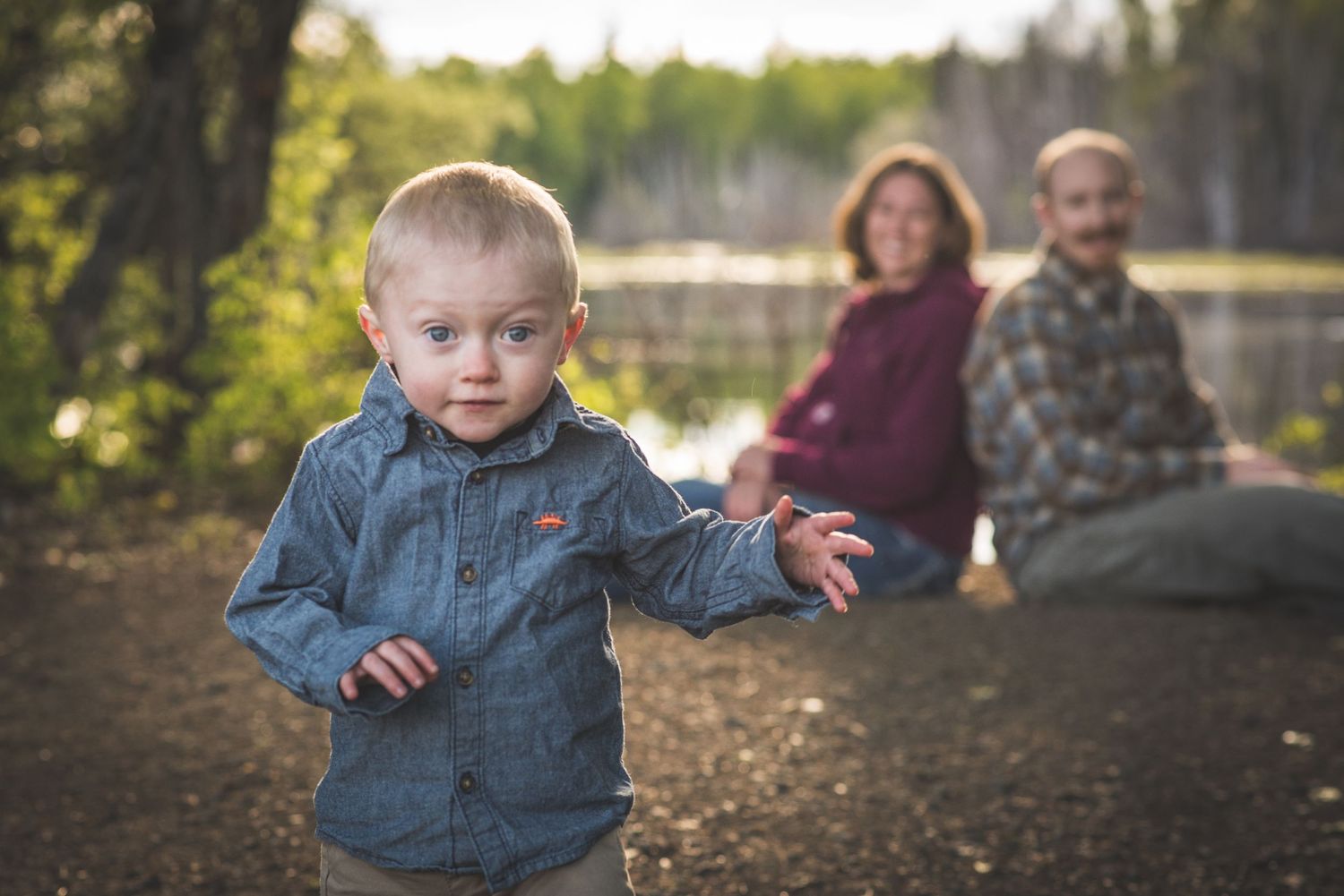Playful toddler exploring outdoors with family in background. Whitney McLaren Photography