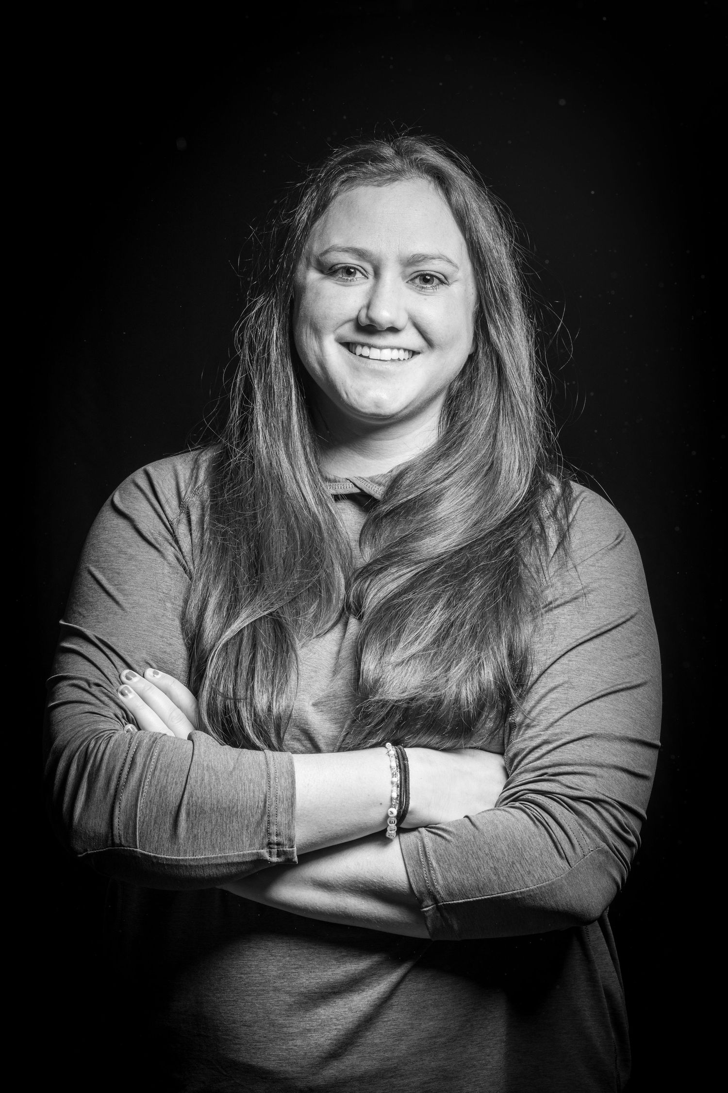 Black and white portrait of a smiling woman with long hair, arms crossed, wearing a casual top.