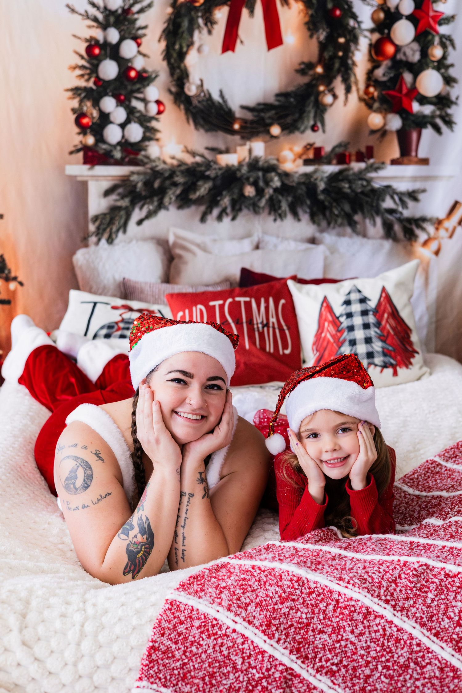 Smiling mother and daughter in Santa hats lying together on bed with Christmas decorations.