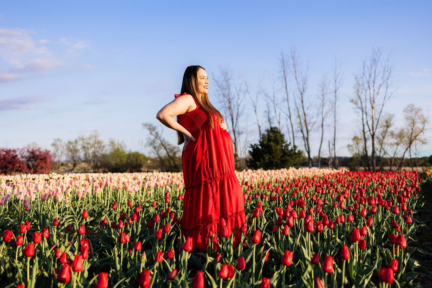 Woman in red dress standing in vibrant tulip field under blue sky.