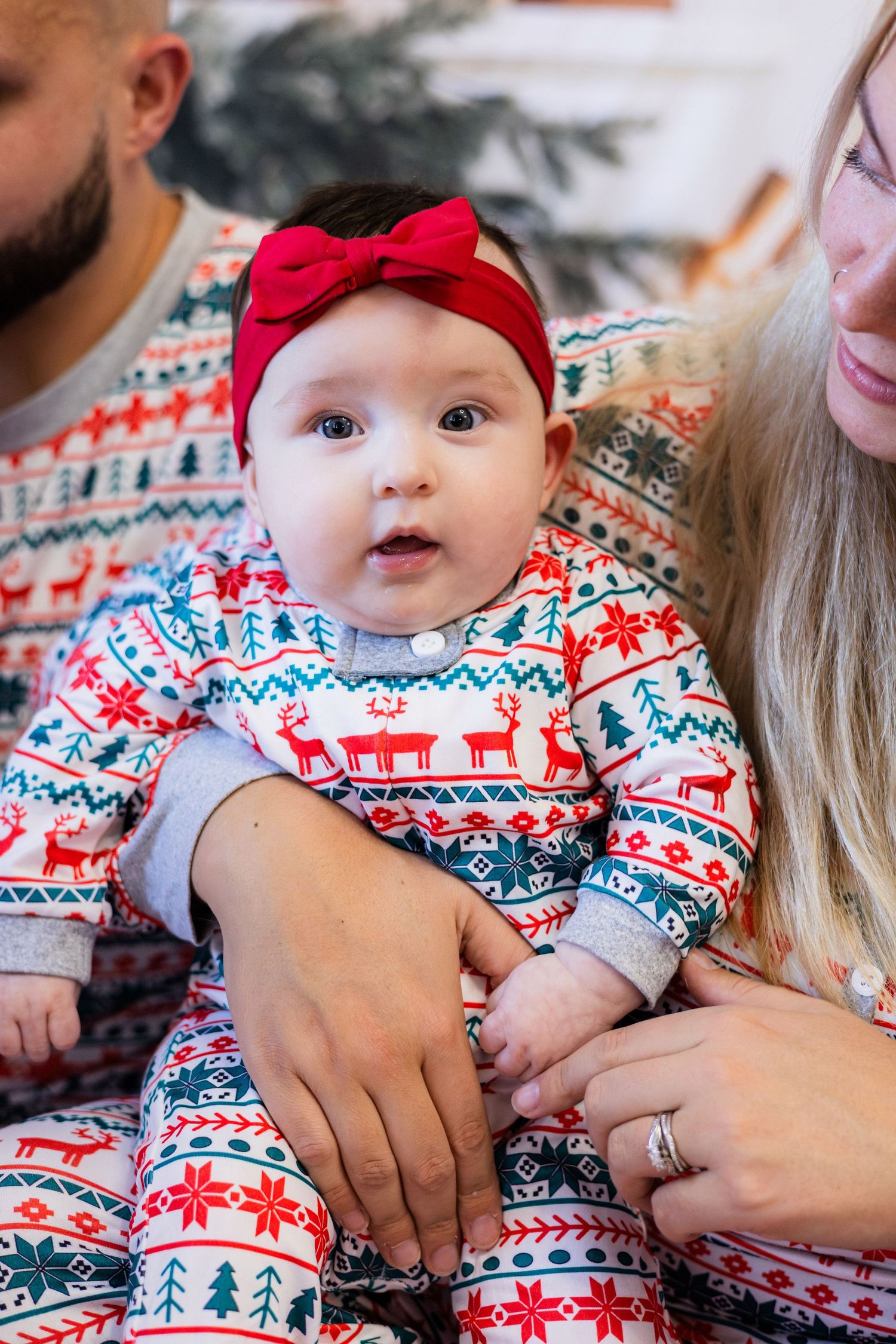 Cute baby girl in matching family Christmas pajamas with red bow headband during holiday photo session.