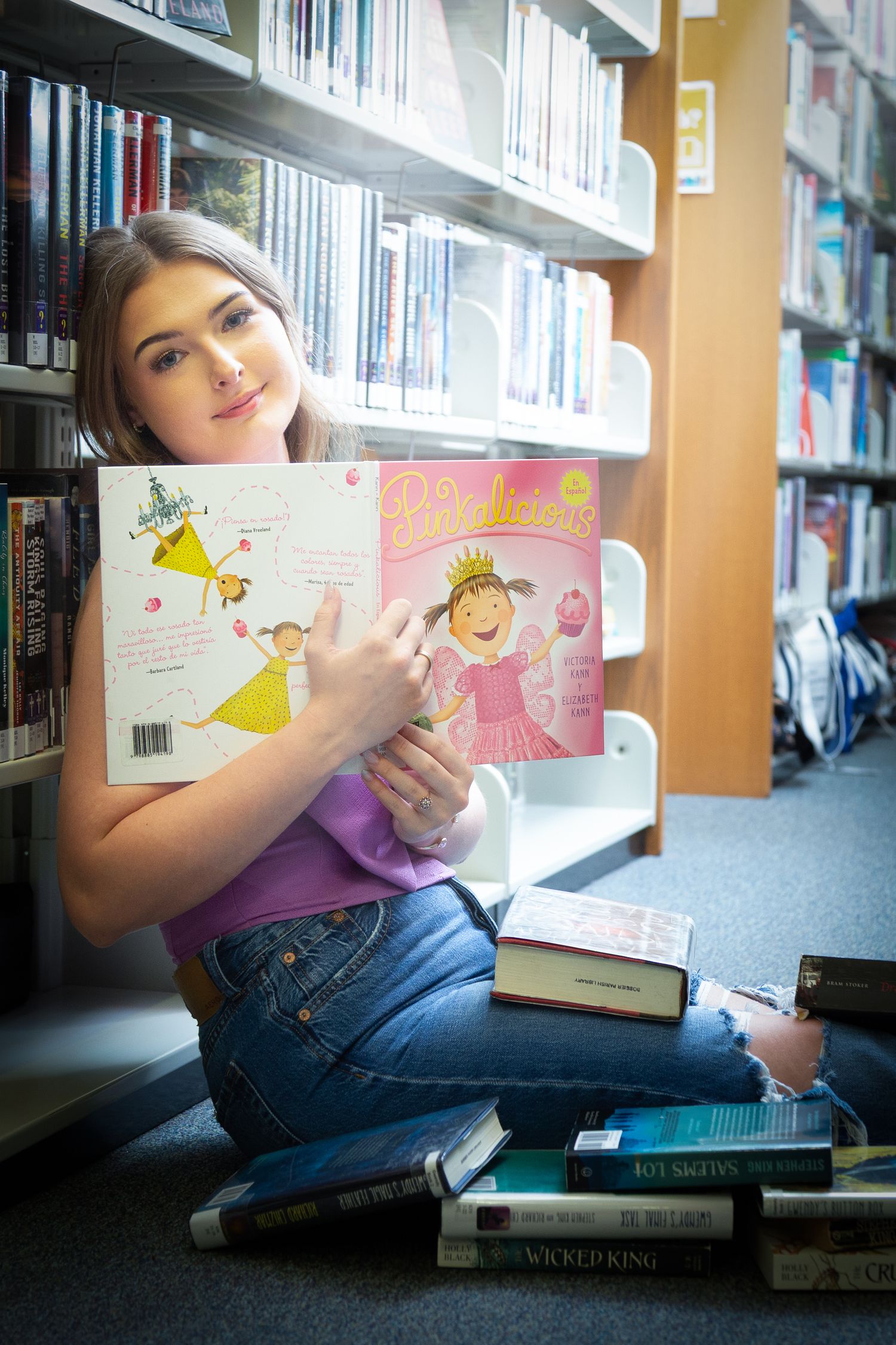 Person lying on floor in library reading a children's picture book among bookshelves.