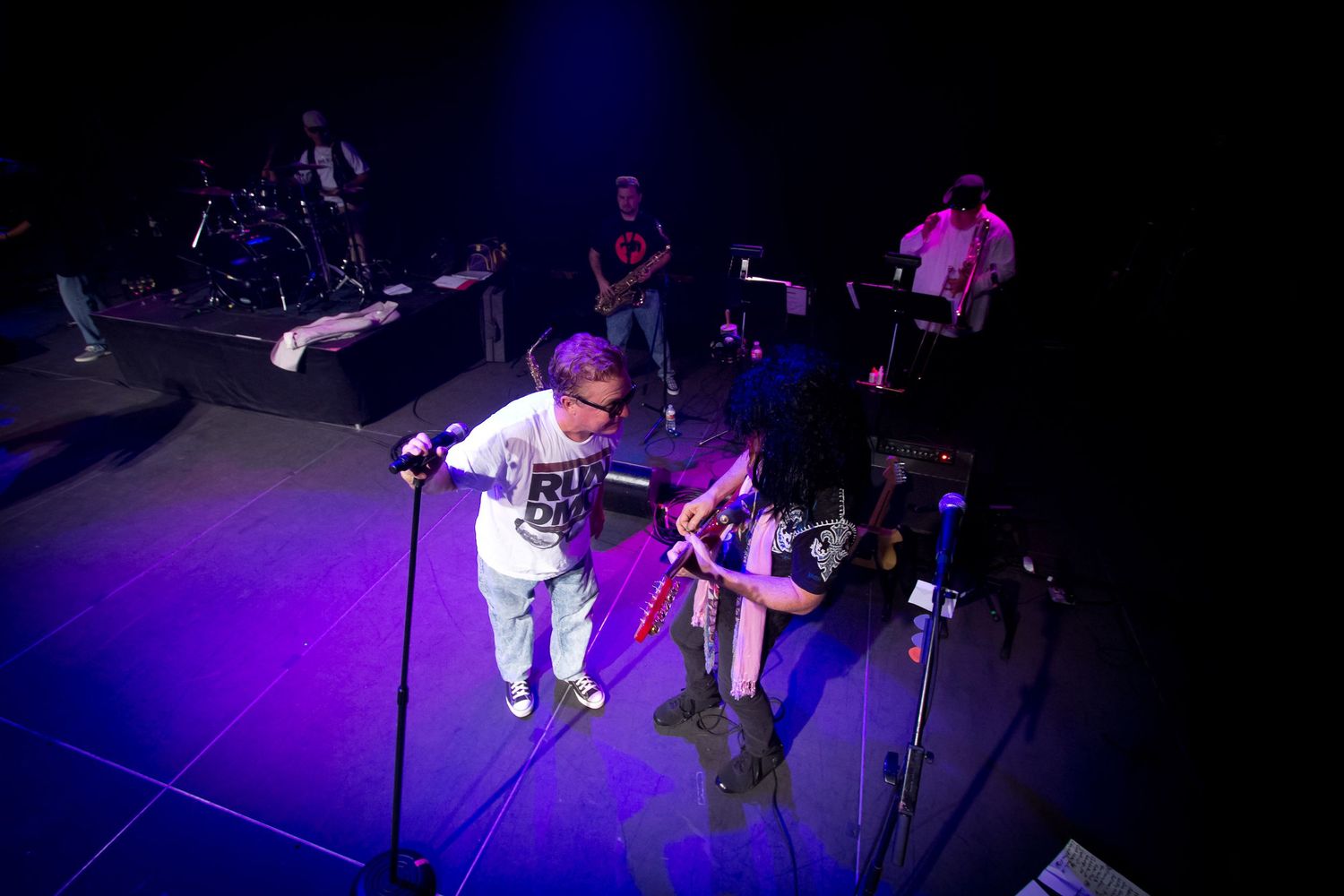 Band performing on a purple-lit stage viewed from above during a live indoor concert.