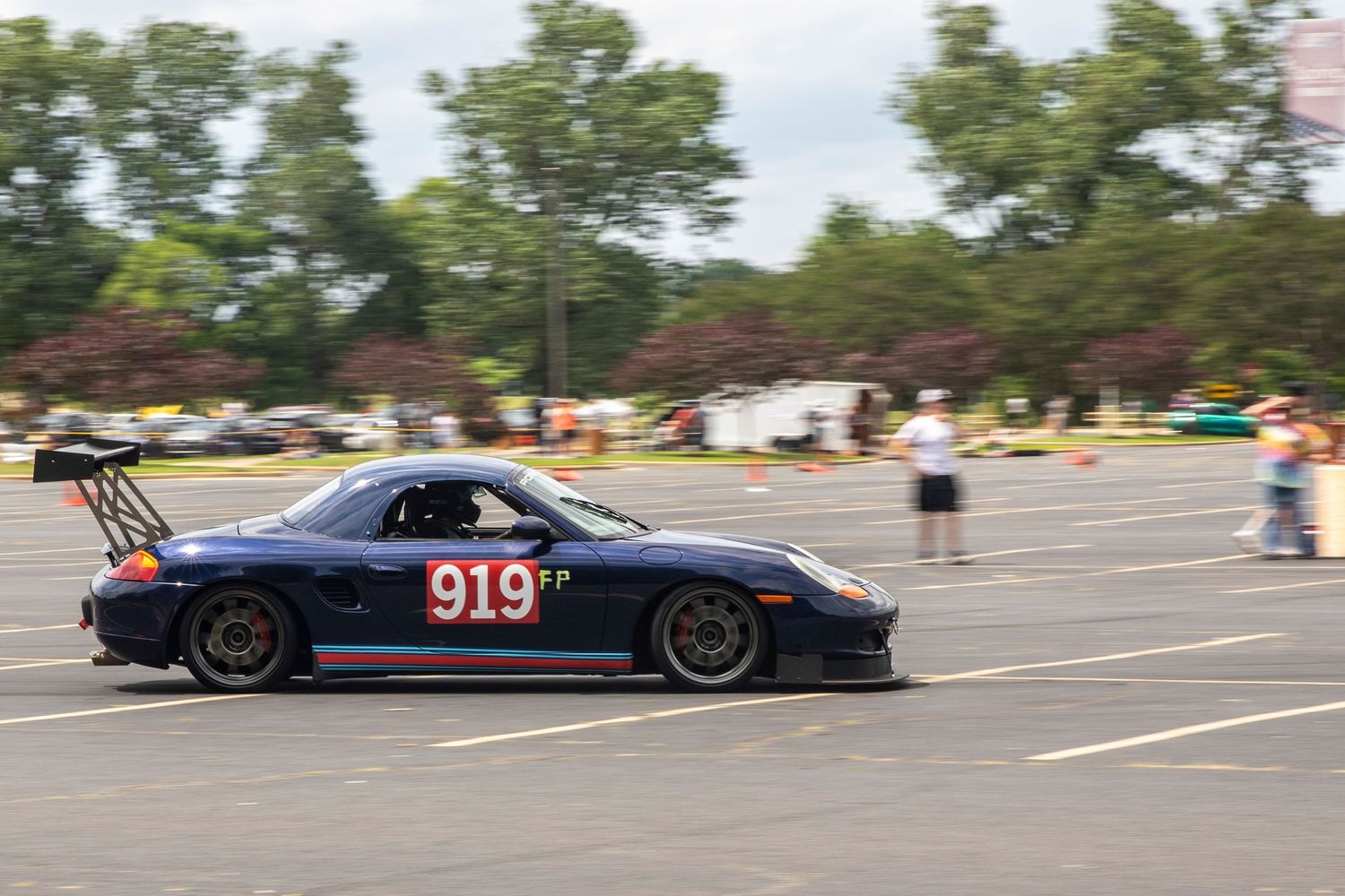 Blue Porsche 919 race car competing in an autocross event on a parking lot course with orange cones.