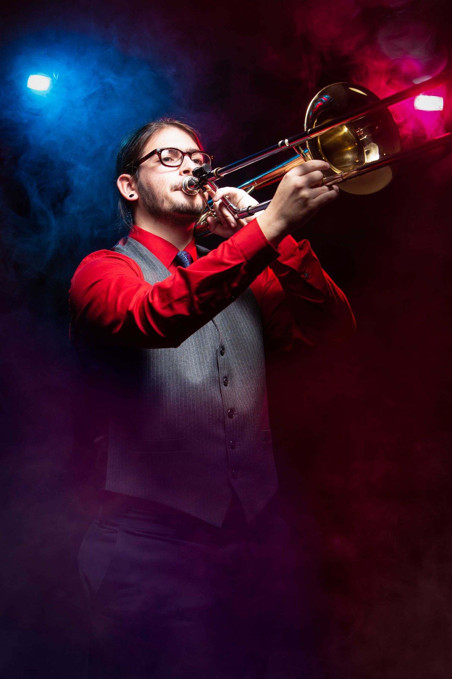 Trumpet player in red shirt performs on stage with dramatic blue and pink concert lighting.