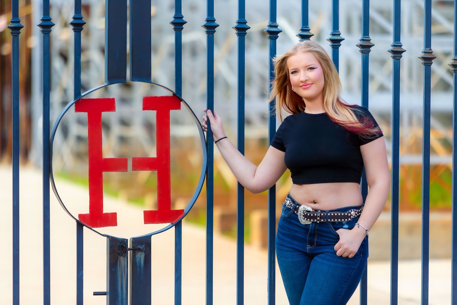 A woman in a black crop top poses outdoors against decorative metal railings with blurred background scenery.