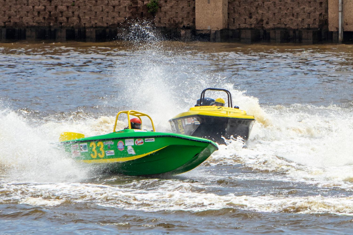 Two colorful racing speedboats, green number 33 and yellow, competing at high speed on choppy water with dramatic splashes.