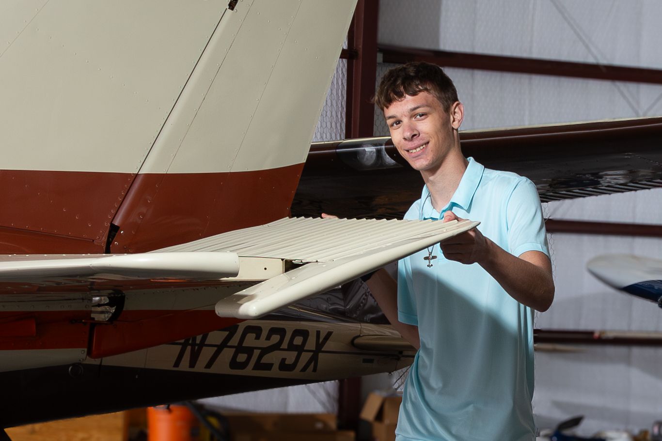 Person in light blue shirt inspects the wing of a small private aircraft in an indoor hangar setting.