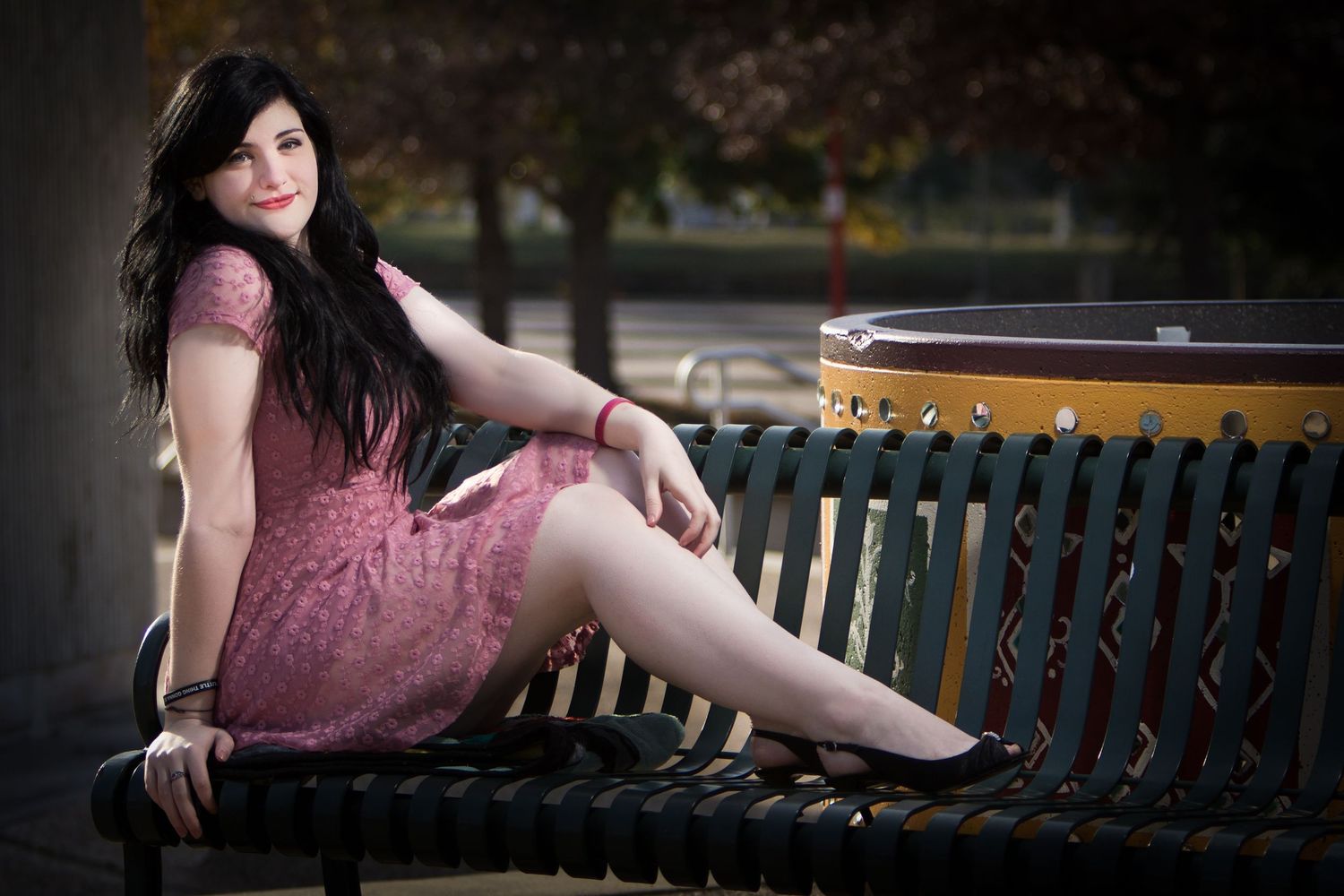 A High School Senior from Shreveport Louisiana in a pink lace dress poses on a park bench during an outdoor portrait session.