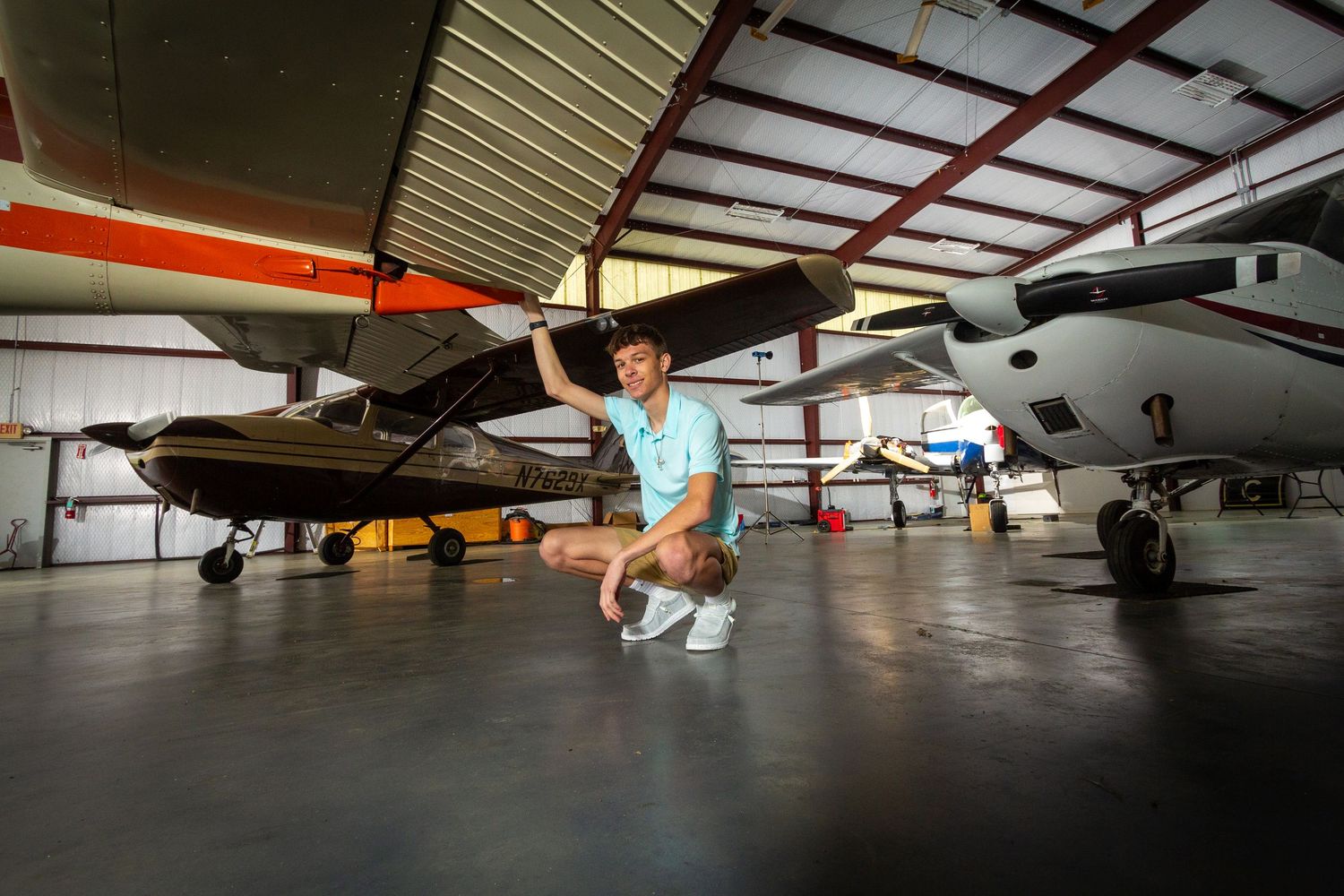 Small aircraft parked in a dimly lit hangar with fluorescent lighting overhead and concrete flooring below.