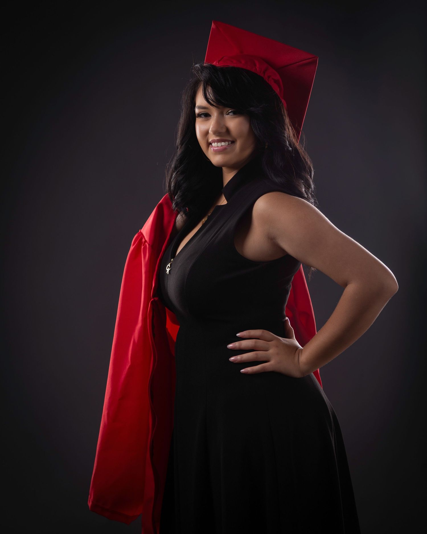 A woman in a black dress and red shawl poses against a dark background in a series of elegant maternity portraits.