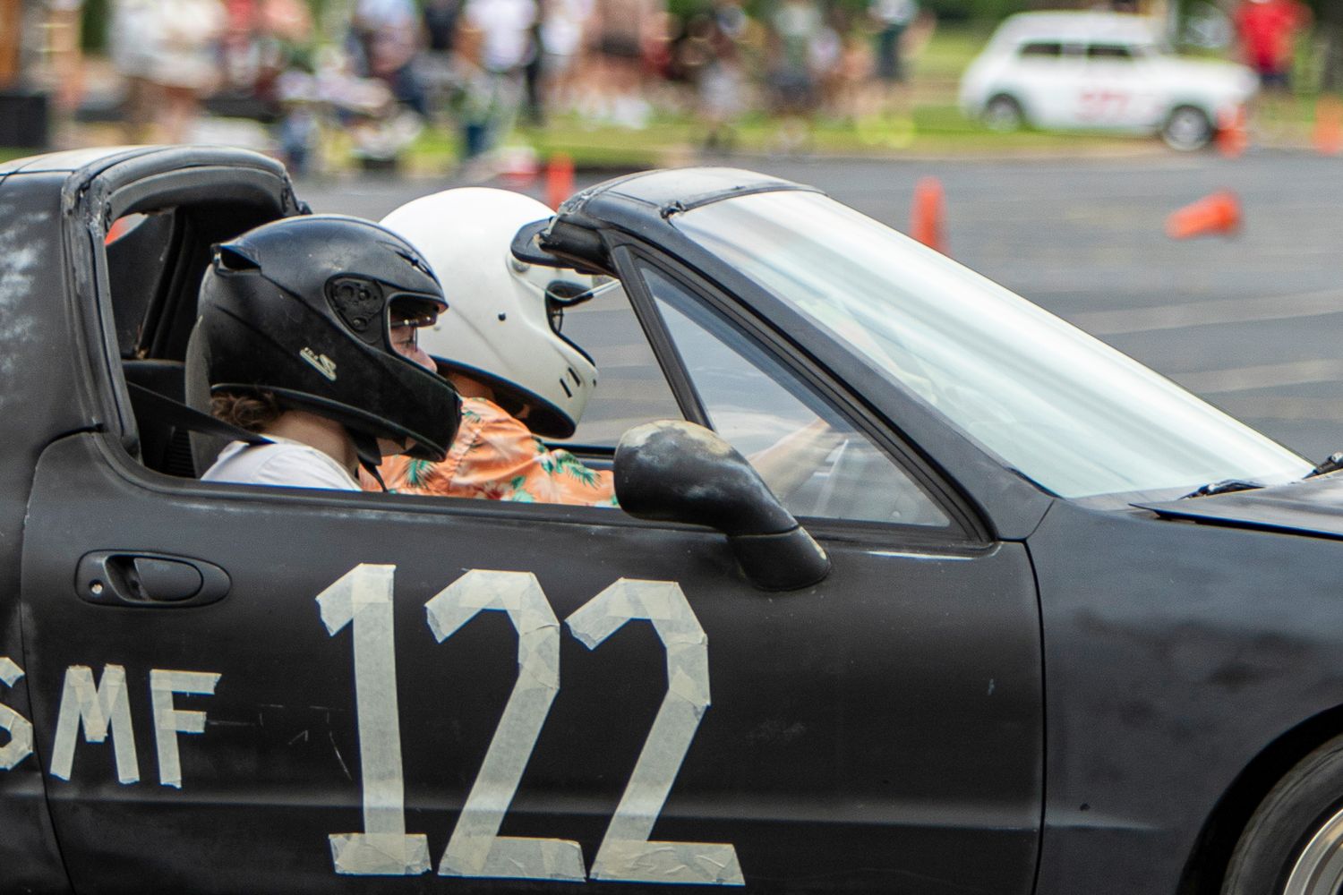Two drivers wearing helmets sit in car number 122 during an autocross racing event on a closed course.