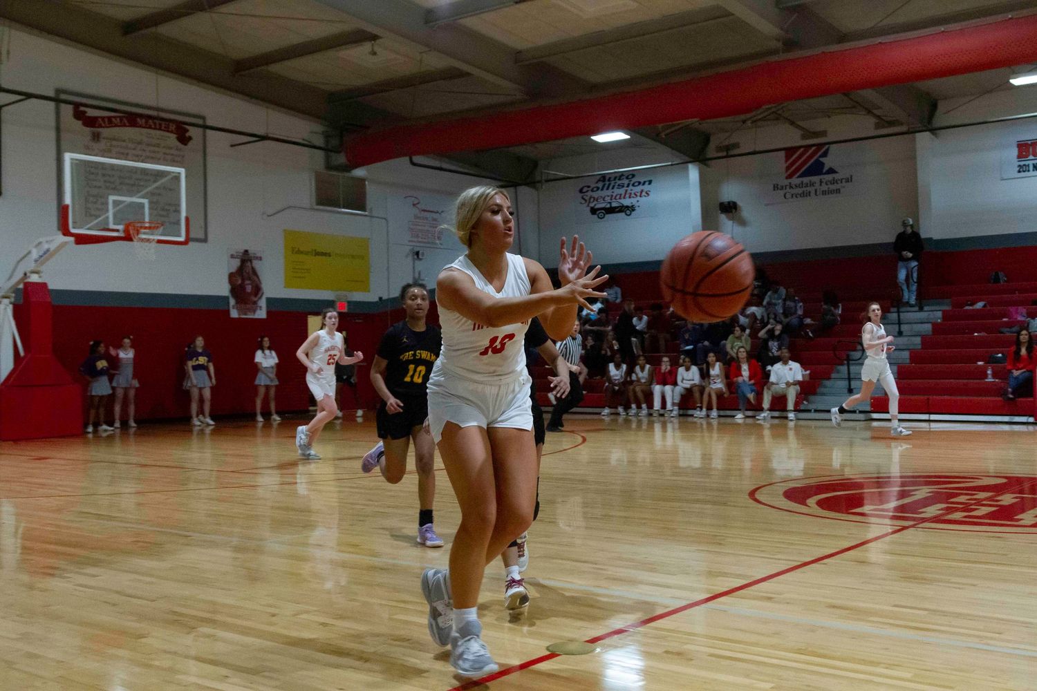 basketball player from Haughton High School in white uniform catches a pass during an indoor high school basketball game on a red court.