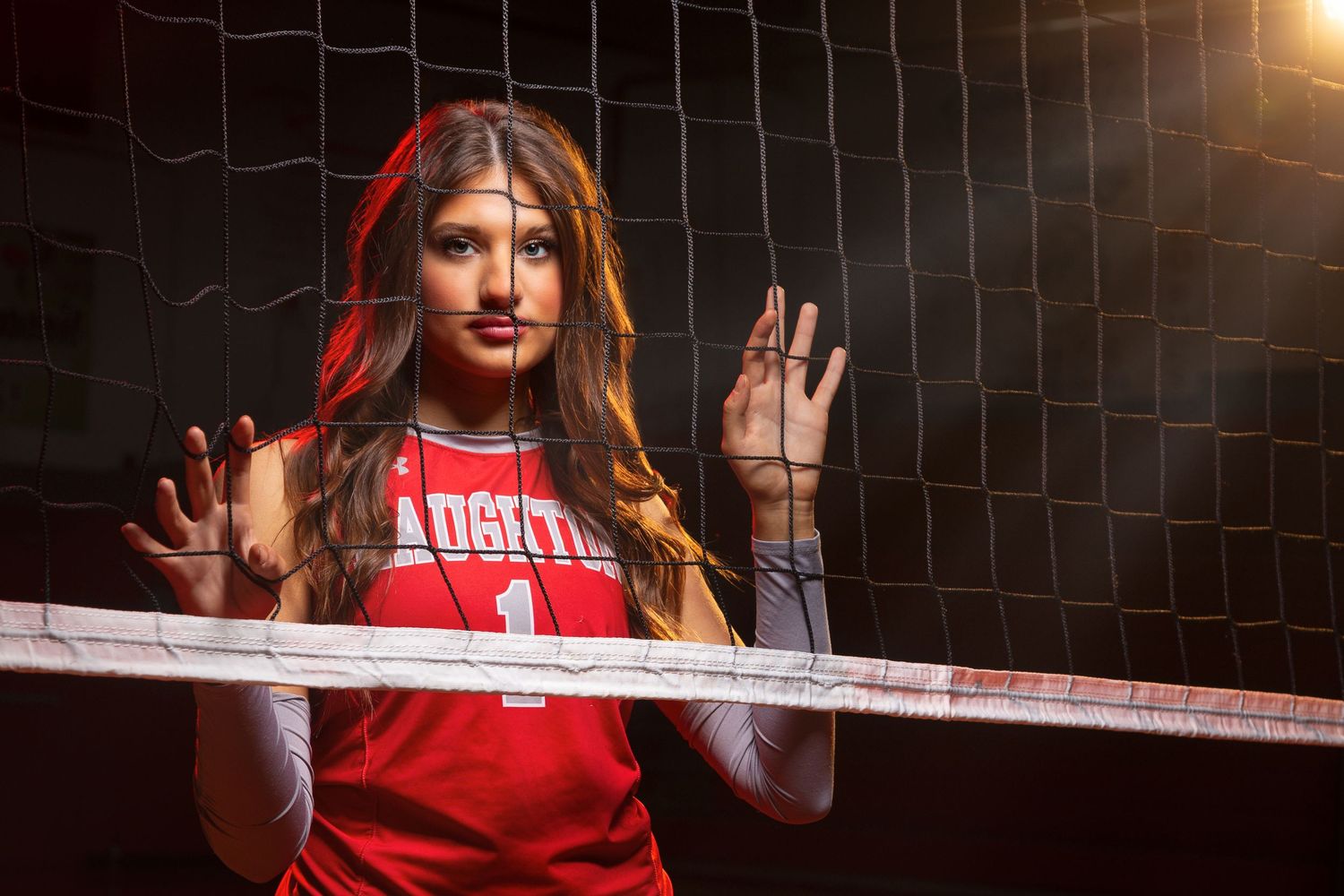 Haughton Louisiana Volleyball player in red uniform poses in front of a net during a photo session with dramatic lighting.