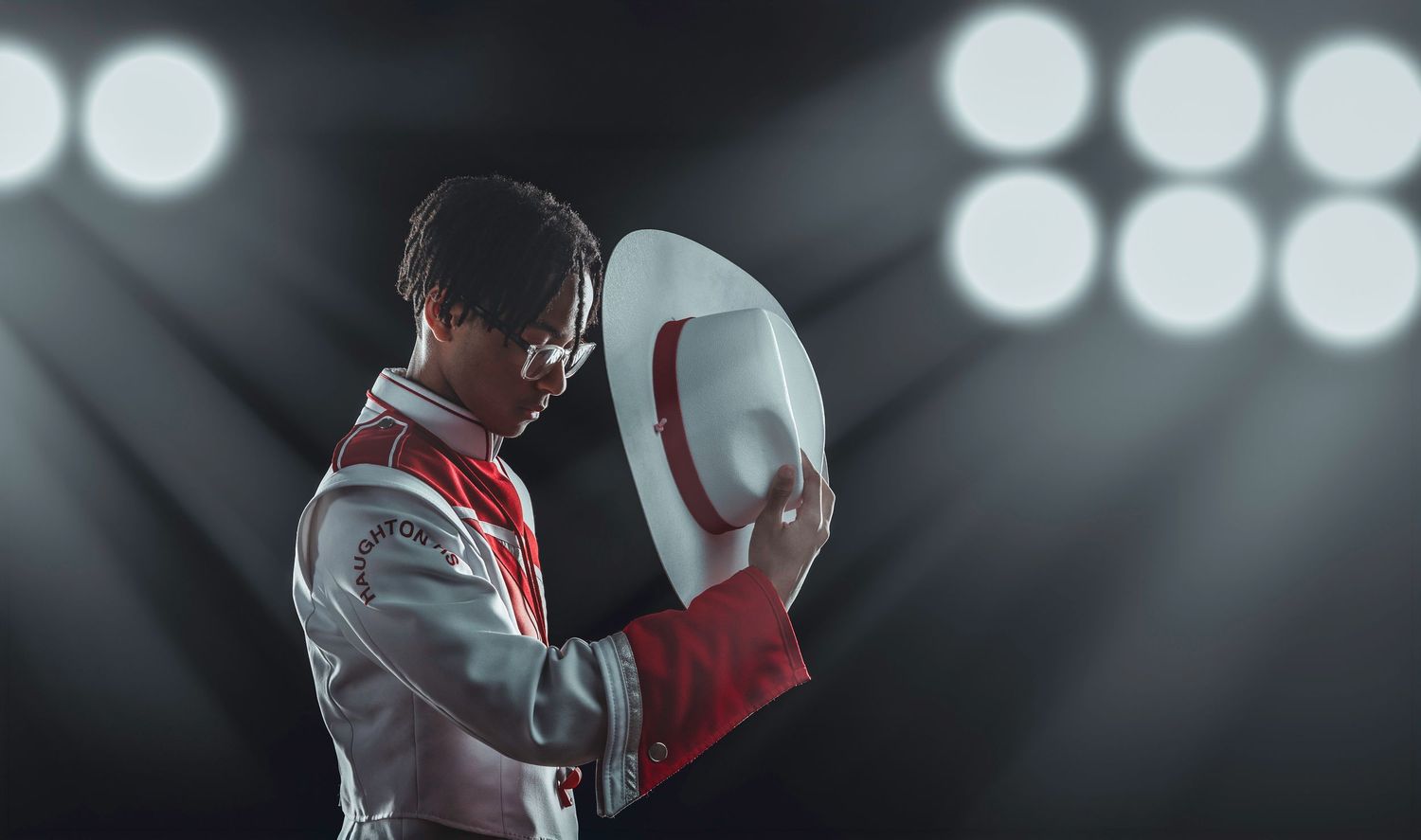 Shreveport Louisiana High School Marching Band Drum Major in white and red outfit holding a cowboy hat under dramatic stage spotlights.