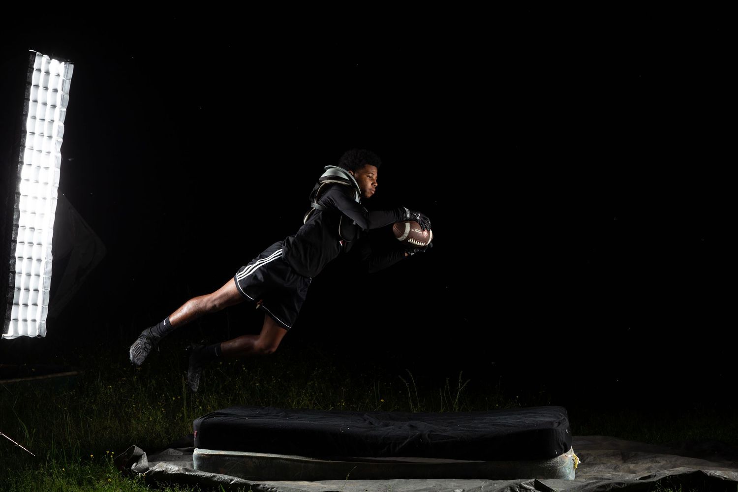 Athlete in black uniform dives dramatically to catch a ball under bright stadium lights at night.