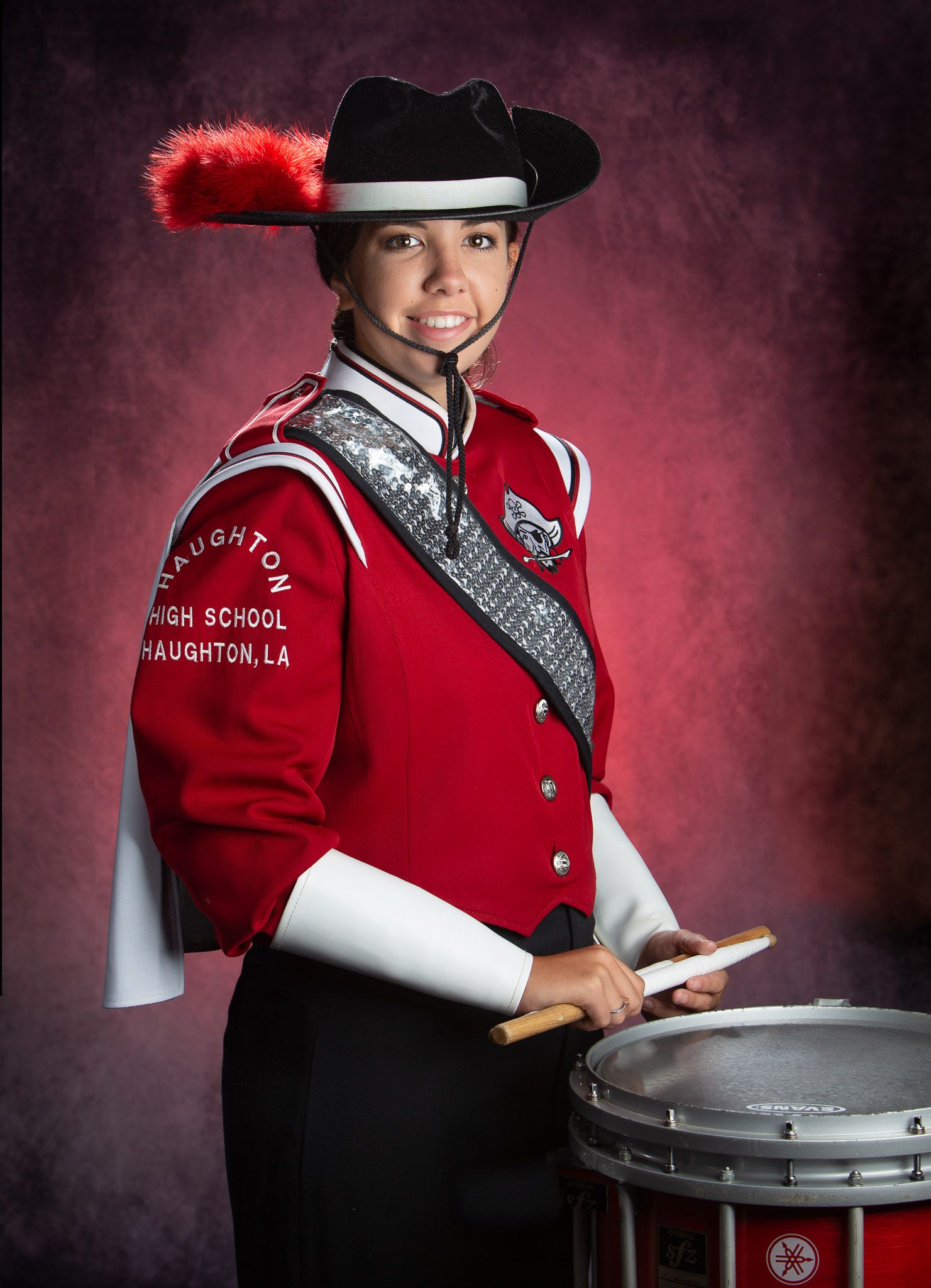 Shreveport High School Marching band drummer in red uniform and black hat poses with snare drum in studio with dramatic red lighting.