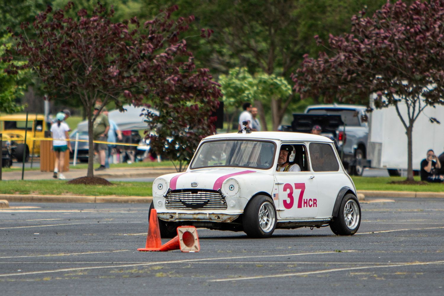 White Mini Cooper race car number 37 navigating autocross course with orange cones in parking lot.