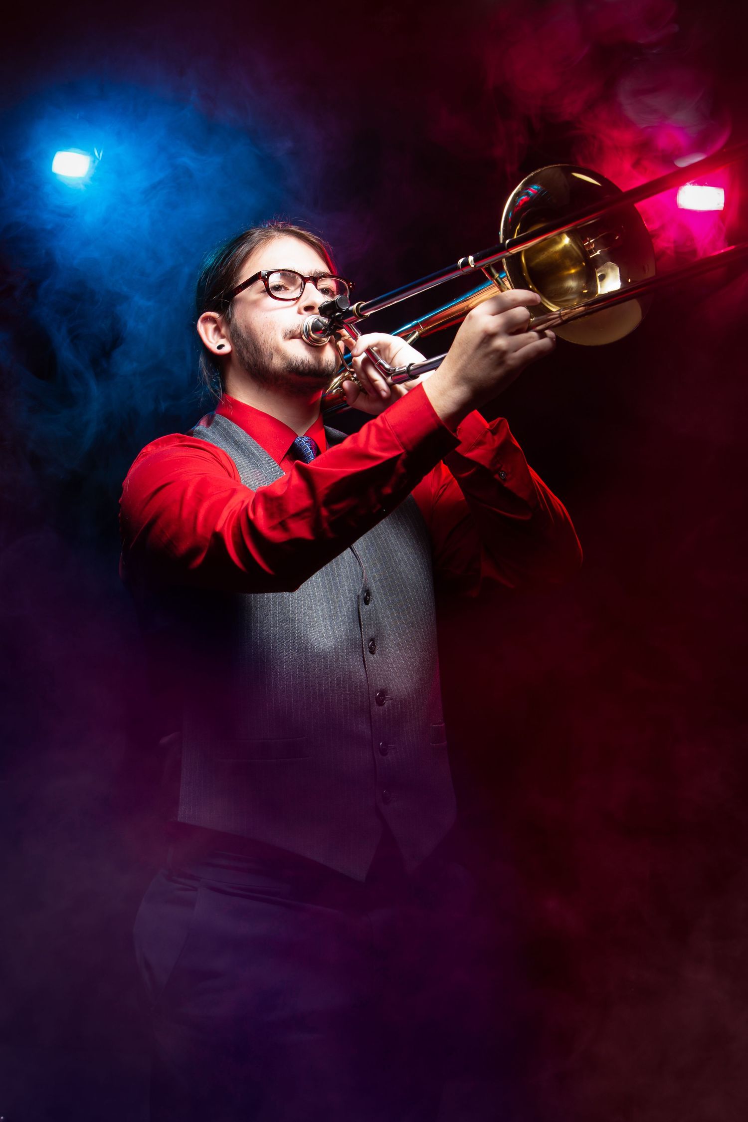 Shreveport Musician in red shirt plays trumpet against dramatic blue and red stage lighting in moody performance series.