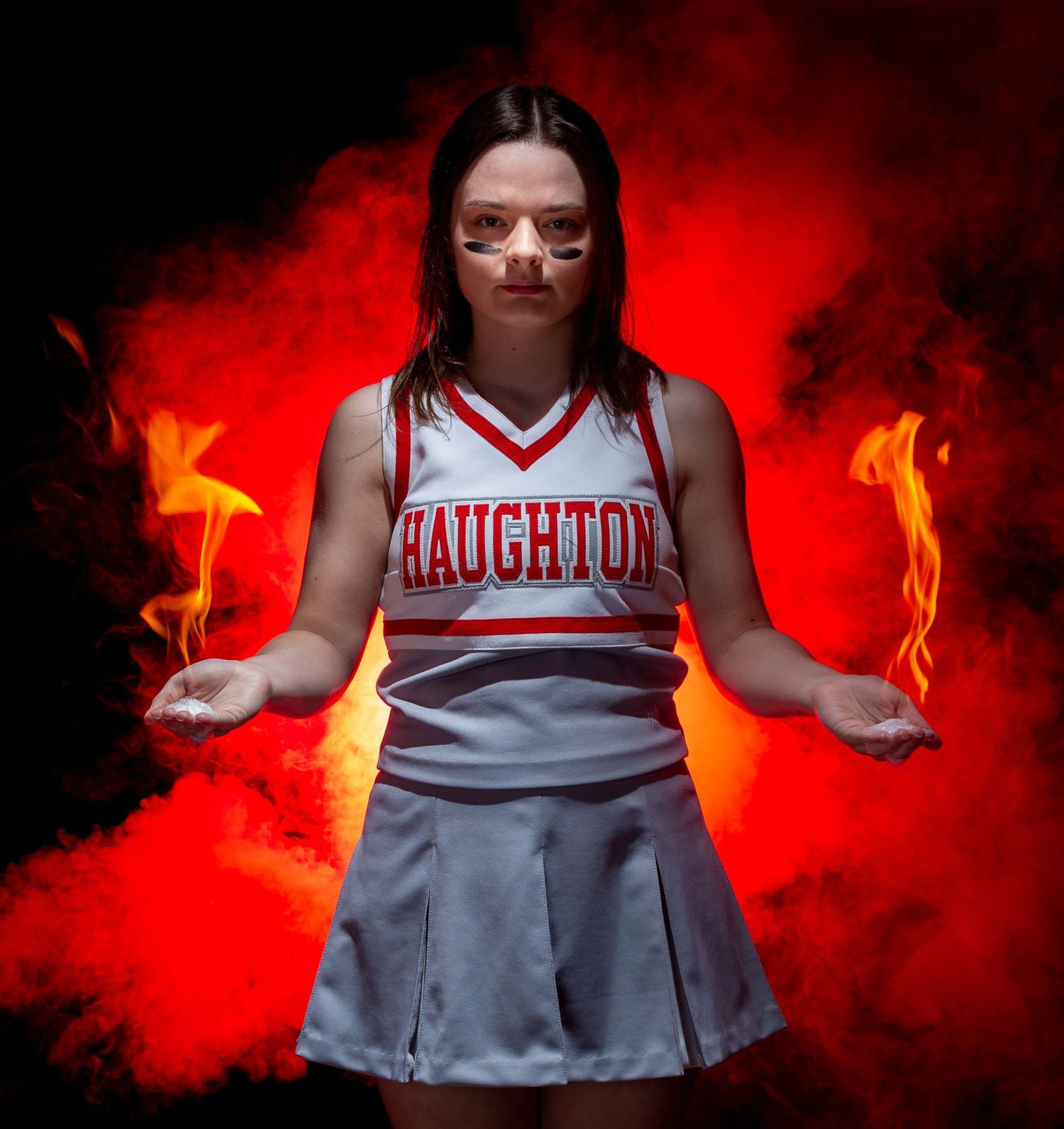 A cheerleader in red and white uniform poses dramatically against a dark background with red smoke effects.