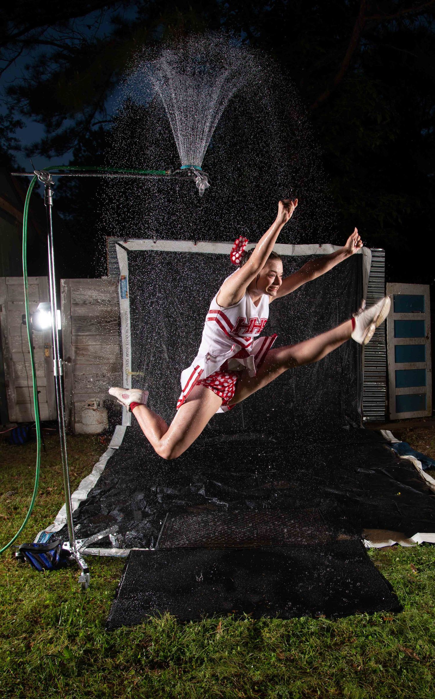 Haughton Louisiana High School Cheerleader in red and white uniform leaping mid-air at night with water fountain spray backdrop outdoors.