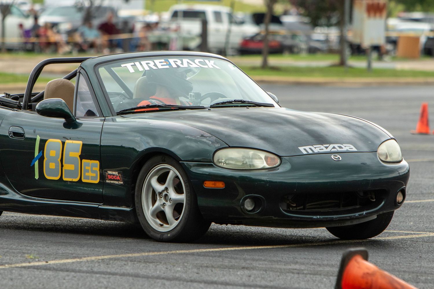 Green Mazda Miata number 85 competing in a Tire Rack autocross racing event on a parking lot course.