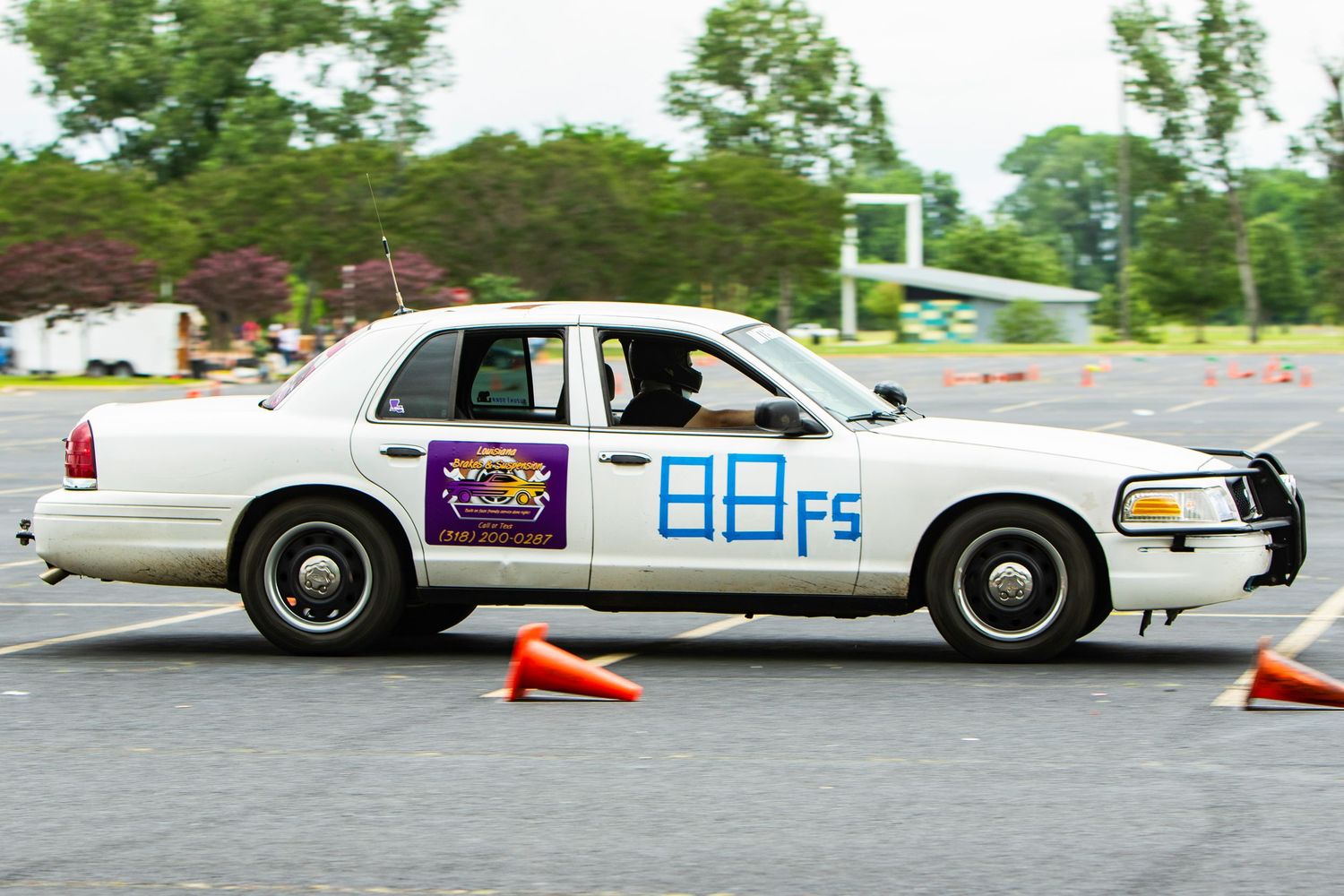 White Ford Crown Victoria race car #88FS navigating orange cones on an autocross course during a motorsport competition.