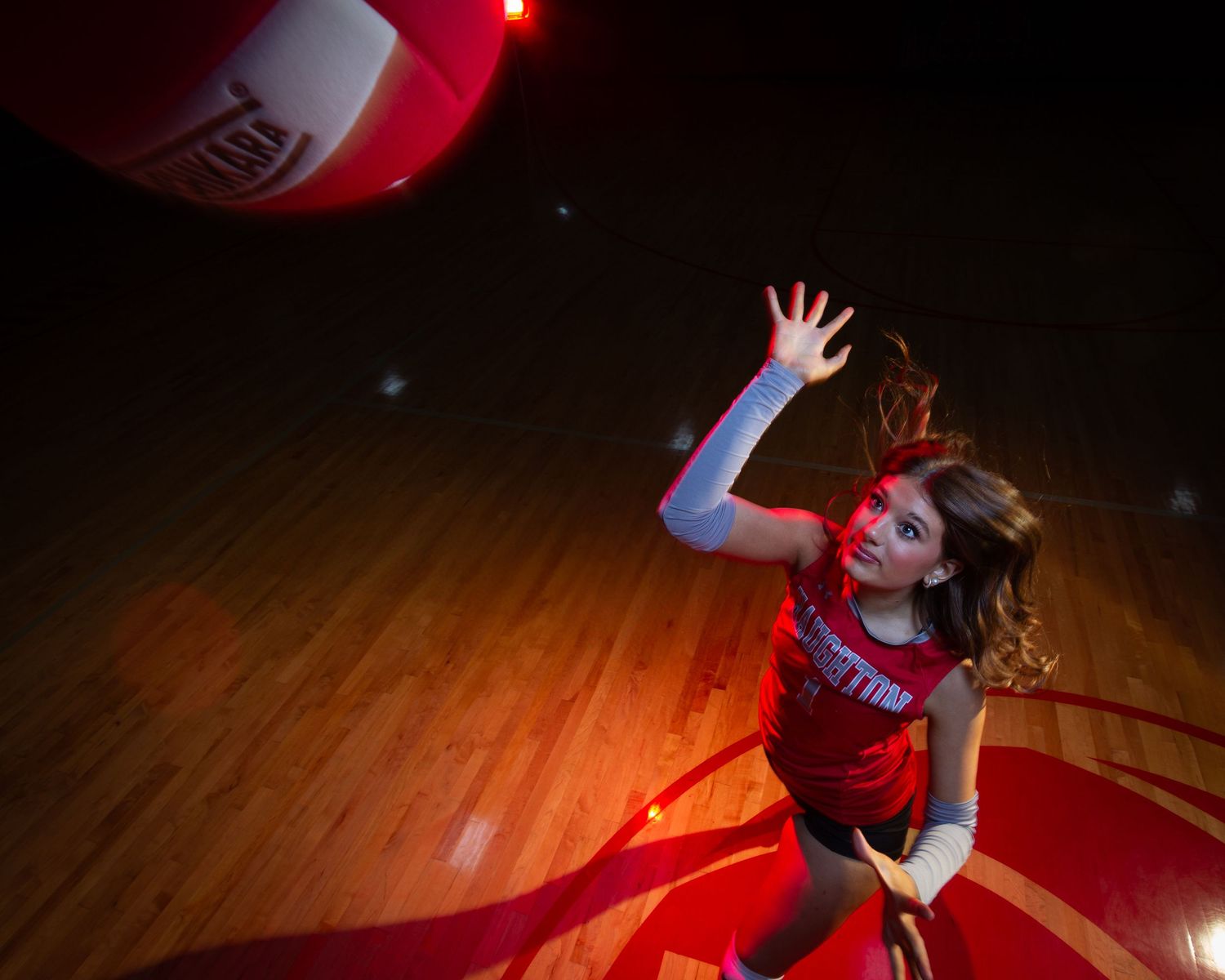 A dancer in red lighting performs an expressive contemporary dance movement on a dark wooden floor.