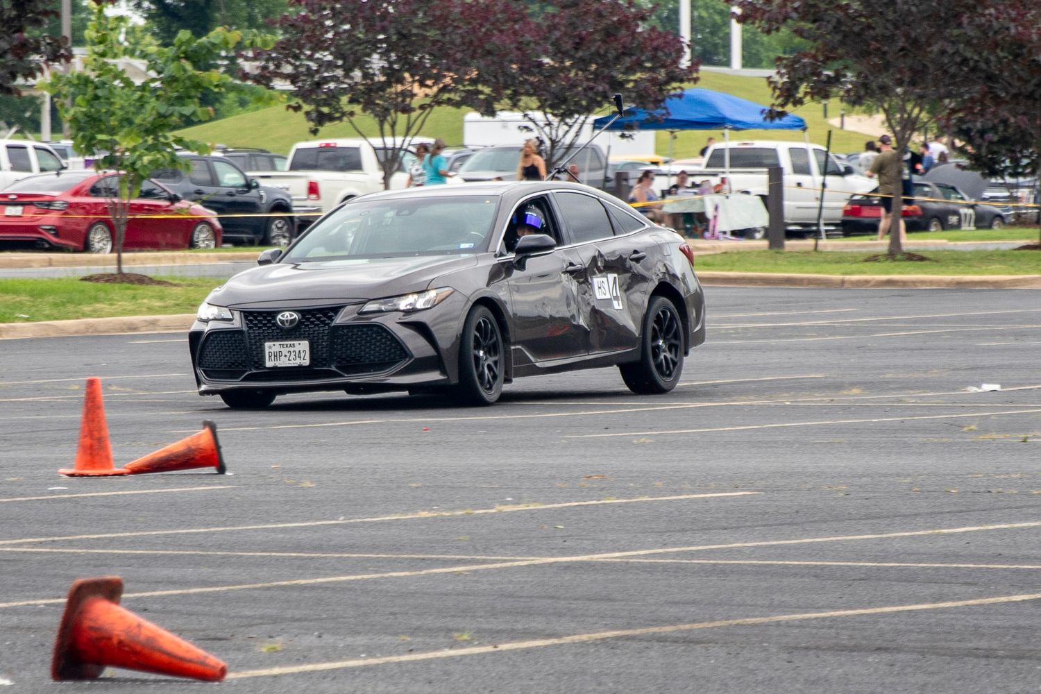 Dark gray Toyota sedan navigating orange cones in a parking lot autocross event on a sunny day.