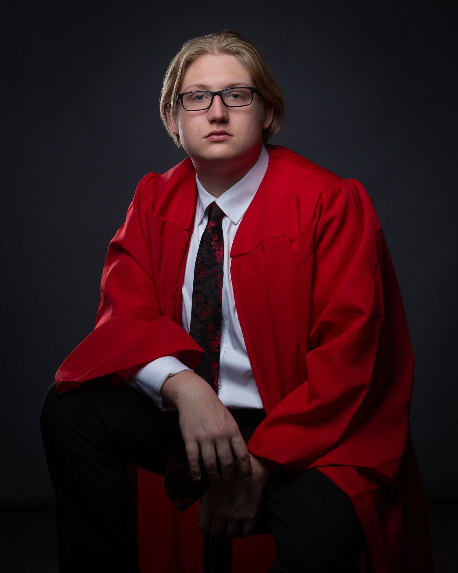 Professional high school senior portrait series showing person in red graduation gown and black tie against dark background.