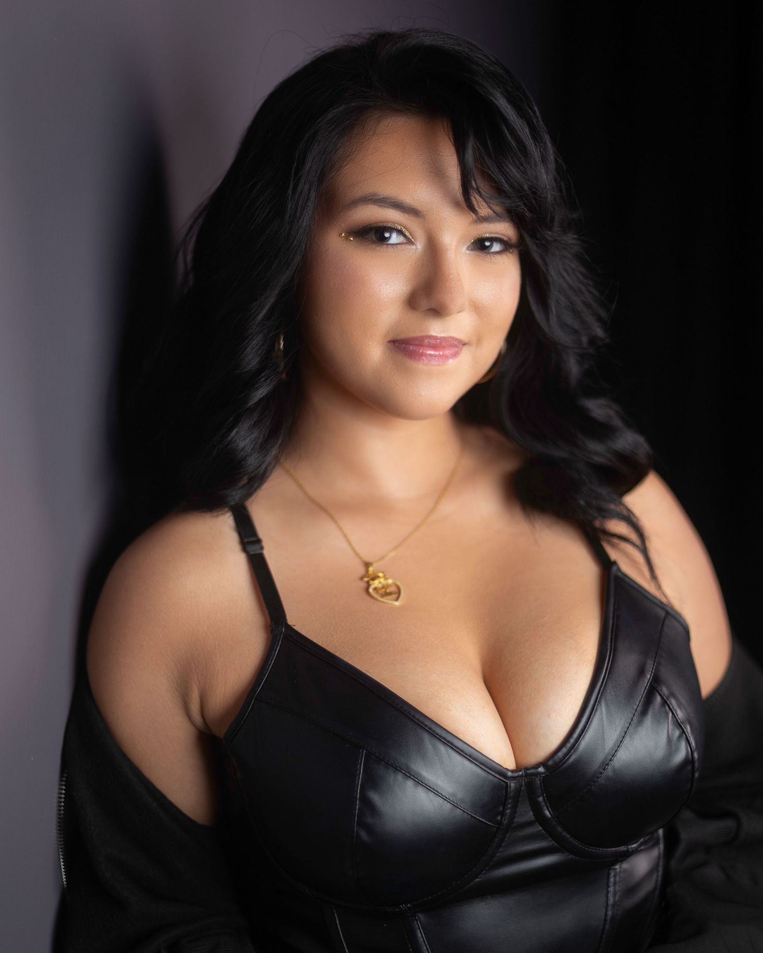 A woman in black poses for a dramatic boudoir photoshoot with soft lighting and shadows.