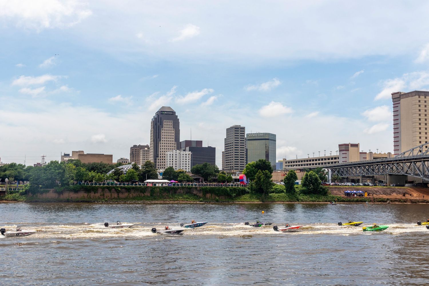 Speedboats race on a river with the Shreveport, Louisiana skyline and blue sky in the background.