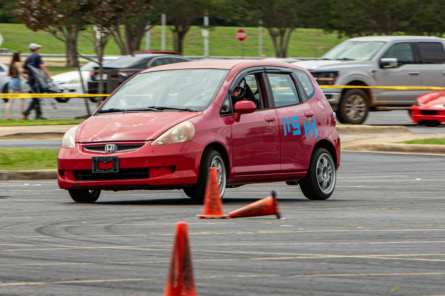 Red Honda Fit navigates orange cones on an autocross course during a competitive motorsport event.