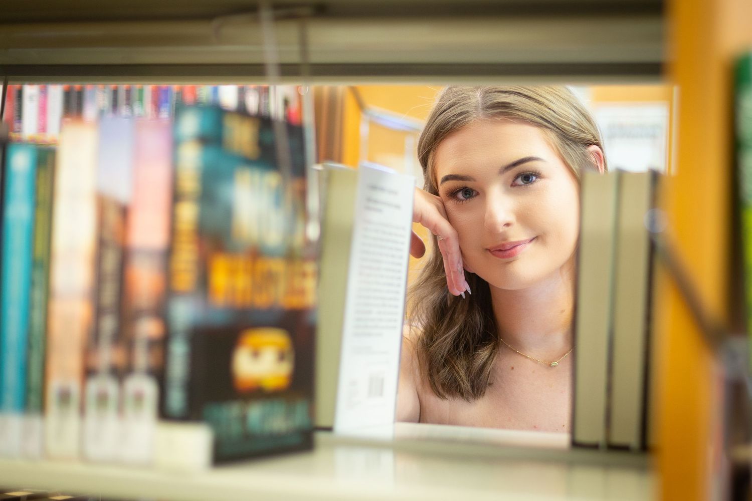 A woman poses in a library setting with bookshelves visible in the background.